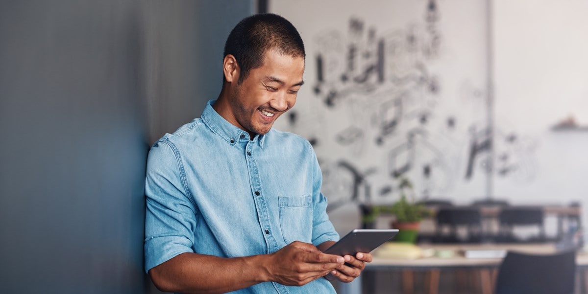 man in office smiling, looking at tablet in hands