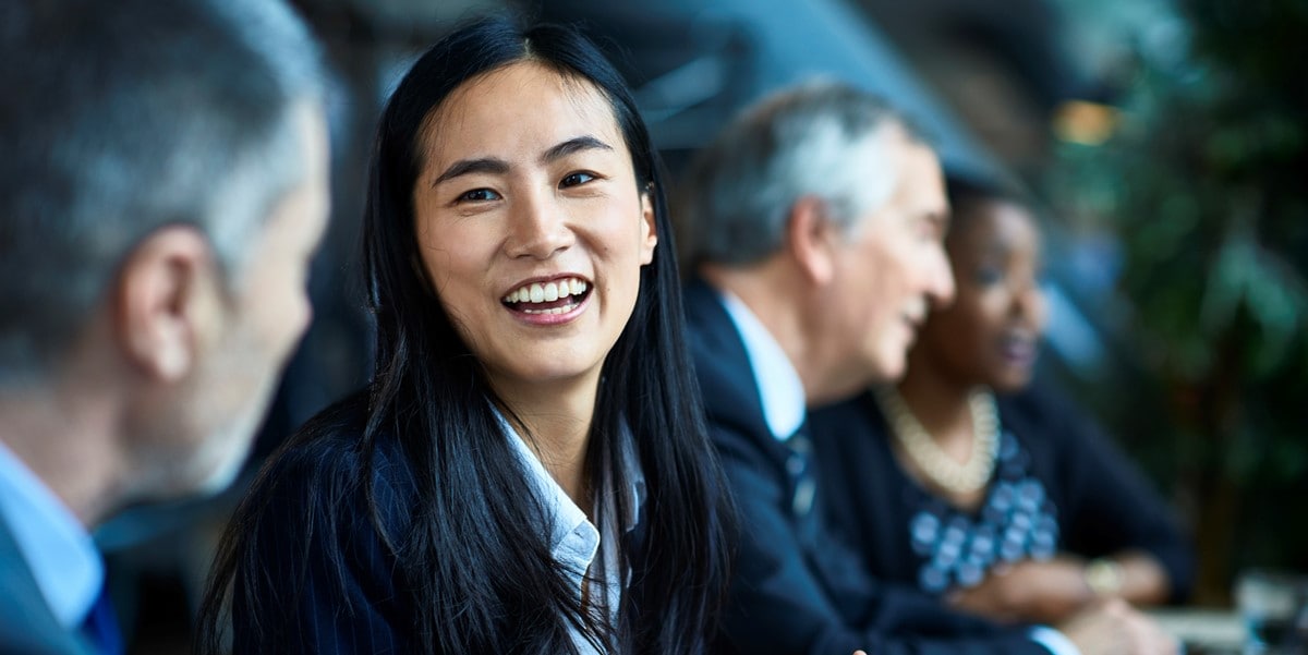 young professional woman smiling, sitting next to colleagues