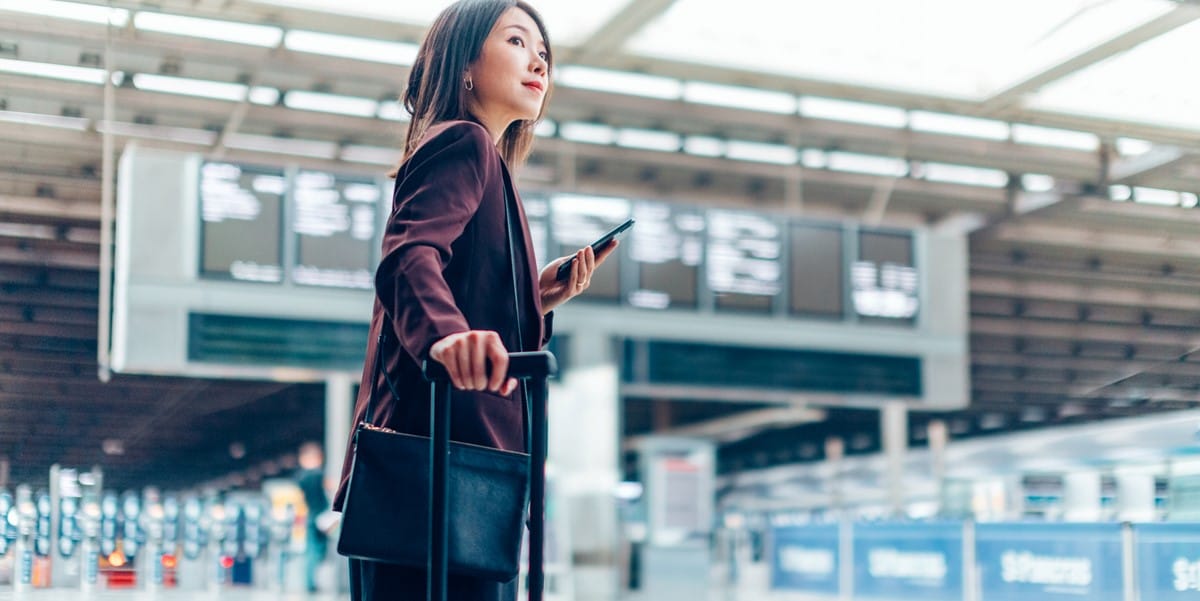 woman at airport with luggage an phone in hand